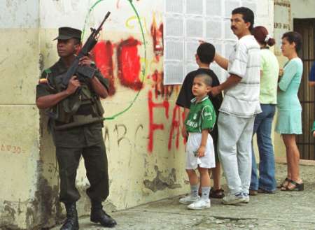 Полицейский стоит на посту, пока избиратели разыскивают свои фамилии 
в избирательном центре президентских выборов в Медельине, 
Колумбия, 26 мая 2002 г. Колумбийцы провели в воскресенье президентские 
выборы в обстановке страха, поскольку, предположительно,  
марксистские повстанцу подвергли бомбардировке избирательный участок, 
убили мэра и заложили автомобильные бомбы в Андском 
национальном сельском наместничестве. Фото и аннотация: Альбейро Лопера, 
агентство Рейтер.  
