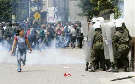Colombian anti-riot police shiled themselves after a small bomb blast while a student runs by 
during a protest by state workers in downtown Bogota, September 16, 2002. Public workers, 
joined by student activists, staged a one-day strike on Monday in the first major challenge 
to new cost cuts set by President Alvaro Uribe to help pay for a military build-up. 
Colombia is gripped by a 38-year-old guerrilla war, and police were told to be on alert for 
possible infiltration by leftist rebels in the Monday protests. REUTERS/Jose Miguel Gomez
