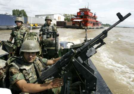 Колумбийские солдаты в патруле на борту быстродействующего бронированного патрульного судна, в портовом городе Маганге в северном департаменте Боливар, на реке Магдалене, рядом с баржей, 30 августа 2002 . Колумбийское правительство тратит 100 миллионов долларов, чтобы модернизировать коммерческую доступность и навигационную оснащенность реки, что очень важно для Колумбии, и для чего также привлекаются услуги Вооруженных сил, позволяющие гарантировать безопасный  от возможного нападения партизан проход для судов. Фото и аннотация: Хосе-Мигель Гомес, агенство Рейтер, пятница 30 августа 2002 г.; 07 ч. 31 мин. всемирного времени.
