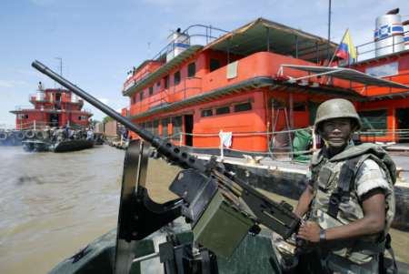 Колумбийский солдат с тяжелым пулеметом в патруле на борту быстродействующего бронированного патрульного судна, в портовом городе Маганге в северном департаменте Боливар, на реке Магдалене, рядом с баржей, 30 августа 2002 . Колумбийское правительство тратит 100 миллионов долларов, чтобы модернизировать коммерческую доступность и навигационную оснащенность реки, что очень важно для Колумбии, и для чего также привлекаются услуги Вооруженных сил, позволяющие гарантировать безопасный  от возможного нападения партизан проход для судов. Фото и аннотация: Хосе-Мигель Гомес, агенство Рейтер, пятница 30 августа 2002 г.; 07 ч. 32 мин. всемирного времени.
