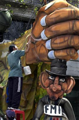 Эквадор, рабочий красит куклу-марионетку с фигурой Эквадорского президента Лусио Гутьерреса, придавленного огромным кулаком, символизирующим Международный Валютный Фонд в Кито. Жители Эквадора традиционно сжигают изображения, обозначаемые как ``Аньос вьехос'', ``Старые года'' в канун Нового года, чтобы избавиться от неудач уходящего года. Фото и аннотация: Долорес Очоа, агентство Ассошиэйтед Пресс, среда 31 декабря 2003 г., 14 ч. 25 мин. всемирного времени.
