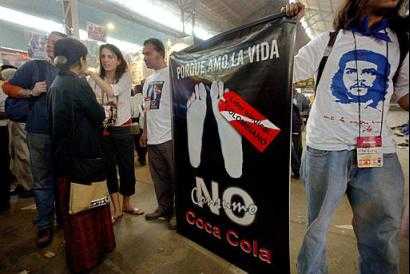 Делегаты из Колумбии протестуют против действий компании Кока-Кола на Всемирном Социальном Форуме в Бомбее, Индия, в воскресенье, 18 января 2004 г. Плакат, написанный по-испански, гласит: ``Так как я люблю жизнь, я не пью Кока-Колу''. Красно-белая бирка в середине плаката на пальце ноги покойника гласит:  ``Колумбийский профсоюзный руководитель''. Фото и аннотация: Маниш Сваруп, Агентство Ассошиэйтед Пресс, воскременье, 18 января 2003 г., 10 ч. 48 мин. всемирного времени