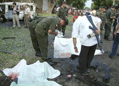 Полицейские осматривают одну из четырех жертв автомобильной бомбы после того, как, предположительно, повстанцы напали на отделение полиции в Кукуте, городе на венесуэльской границе, в 250 милях к северо-востоку от Боготы, Колумбия, в пятницу, 20 декабря 2002 г. Три автомобиля повстанцев, груженых взрывчаткой, добрались до полицейского поста, полиция которого оказала сопротивление, убив одного из нападавших, после чего повстанцы скрылись, оставив автомобиль, заполненный 55 фунтами динамита, который взорвался перед станцией, убив двух полицейских. Фото и аннотация: Эфраин Патиньо, Агентство Ассошиэйтед Пресс; 20 декабря 2002 г., 10 ч. 58 мин. всемирного времени.
