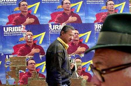 Пешеходы движутся вдоль стенда с плакатами кампании кандидата в президенты Альваро Урибе в Боготе, Колумбии, в пятницу, 24 мая 2002 г. Президентские выборы назначены на воскресенье, 26 мая, и согласно самым последним опросам, Урибе лидирует.   Фото и аннотация: Томас Мунита, агентство Ассошиэйтед Пресс, 24 марта 2002 г. (Надпись на плакате: ``Урибе - президент! Твёрдая рука, большое сердце'' - Рус. ред.)
